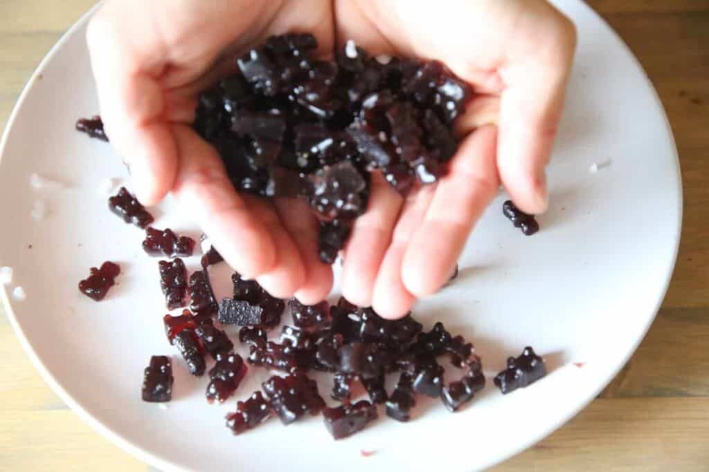 Holding homemade fruit gummies above a white plate.