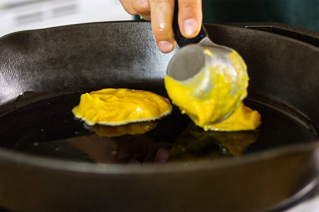 Pouring pumpkin pancake batter into a cast iron skillet.