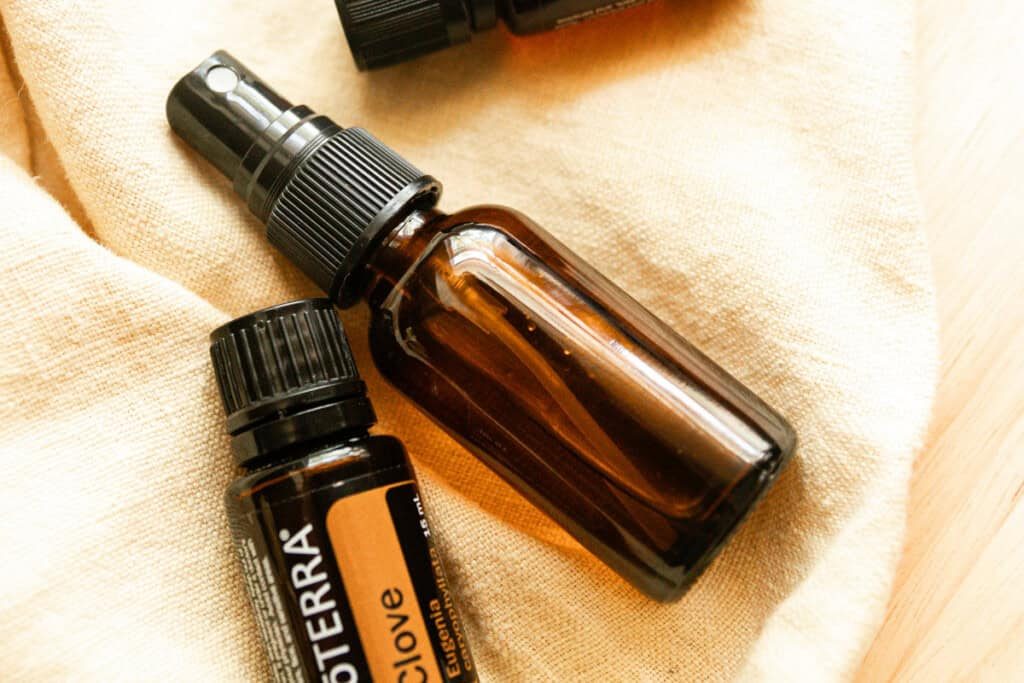 An amber spray bottle with a bottle of clove essential oil on a linen towel.