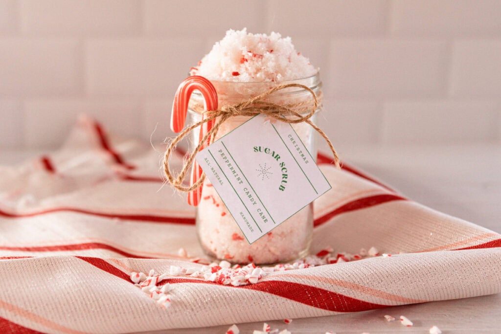 A jar of candy cane sugar scrub on a red and white towel with a candy cane and label tied to the jar.