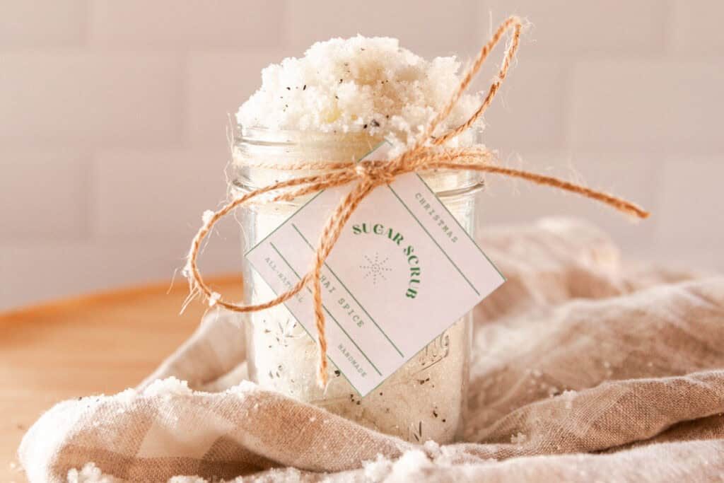 A jar of chai spice sugar scrub with a label tied on with twine and a beige towel.