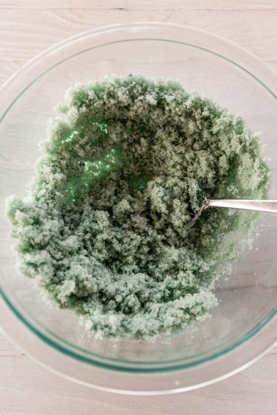 Stirring sugar scrub ingredients in a glass mixing bowl.