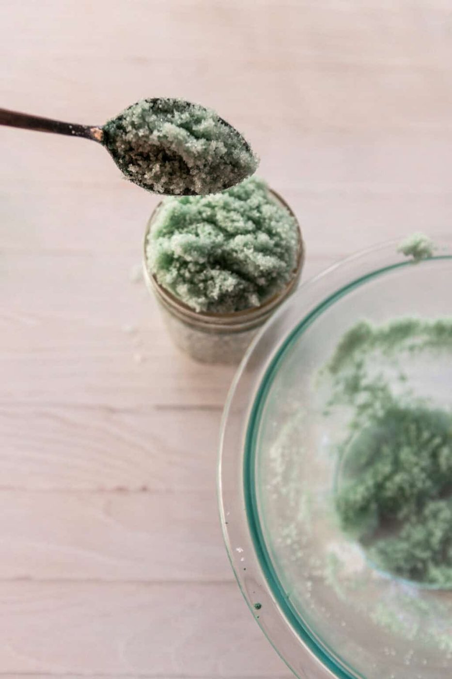 Scooping sugar scrub into a glass jar with a spoon.