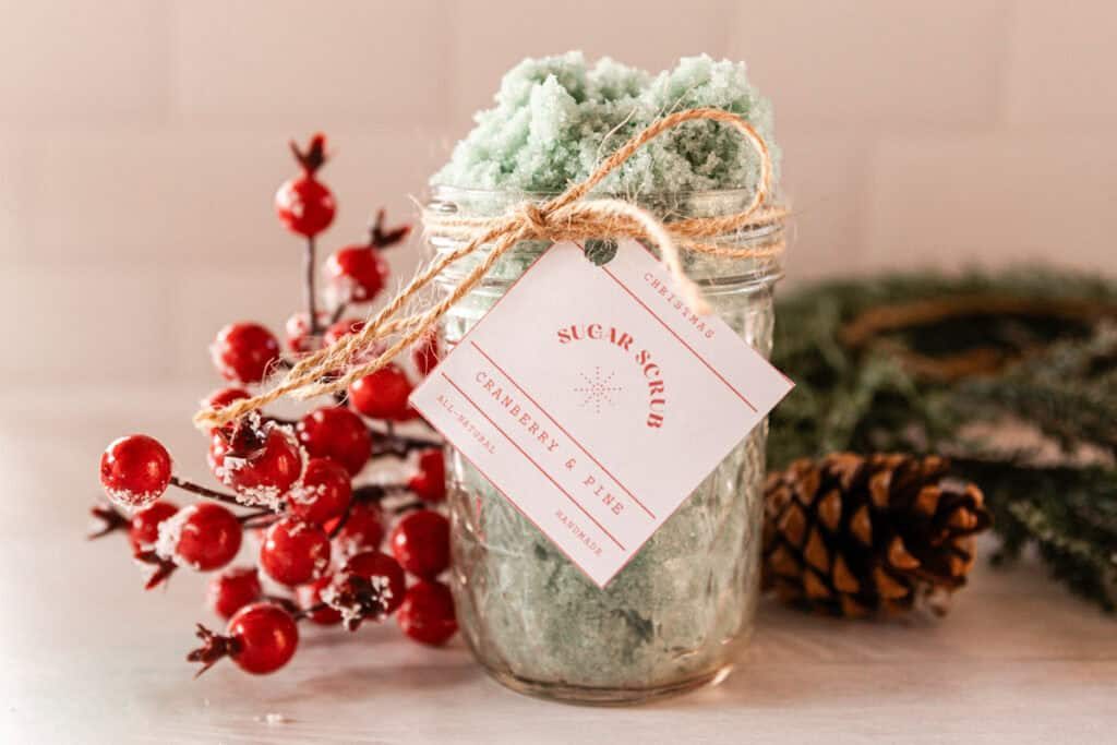 A jar of Christmas tree sugar scrub with pinecones and red berries.