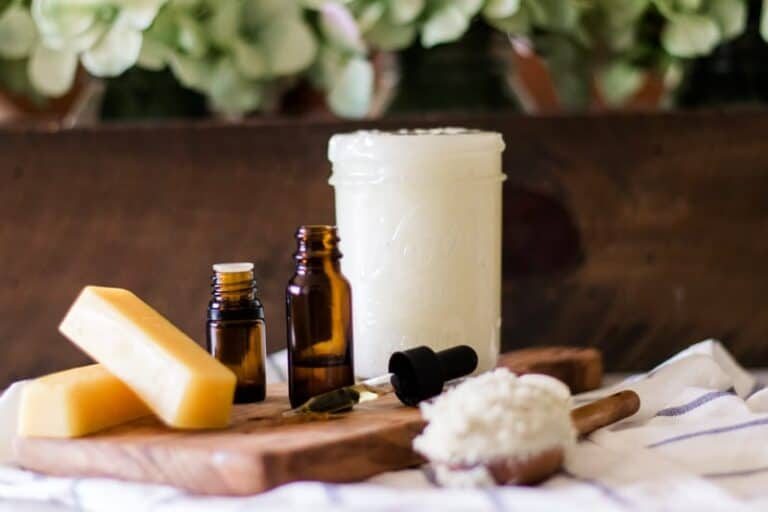 Jar of coconut oil, beeswax, vitamin E oil and essential oils sitting on table.