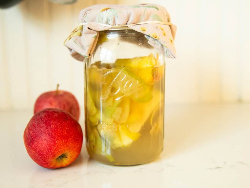 A jar of homemade apple cider vinegar with apples next to it.