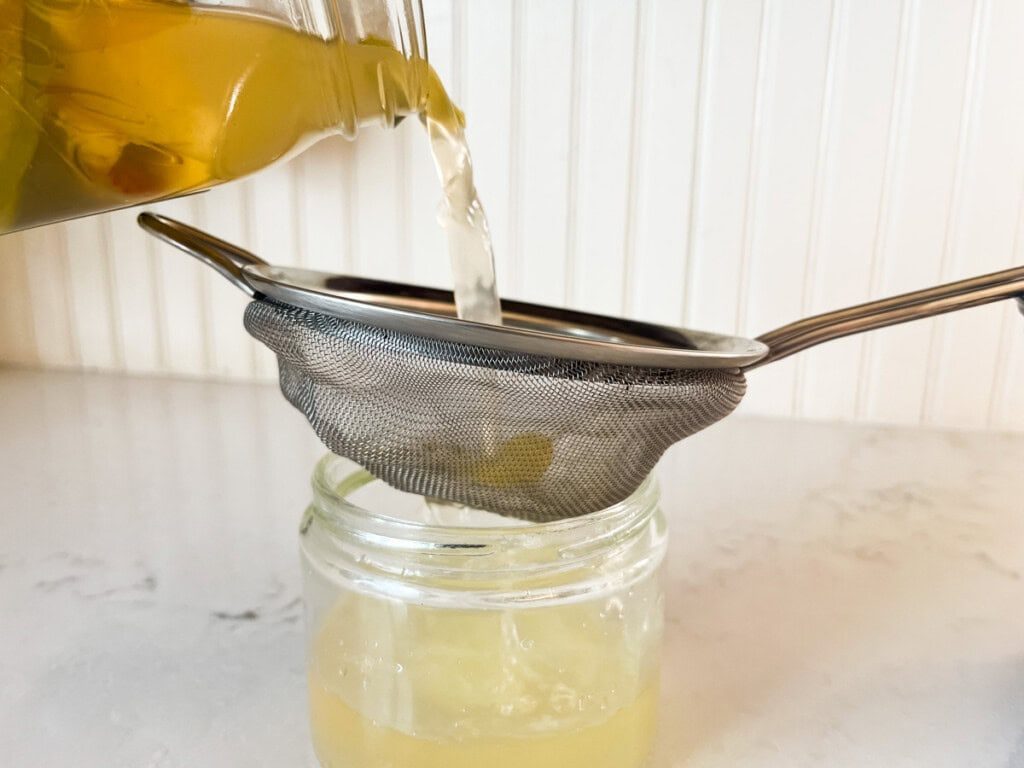 Straining homemade apple cider vinegar through a fine mesh strainer.