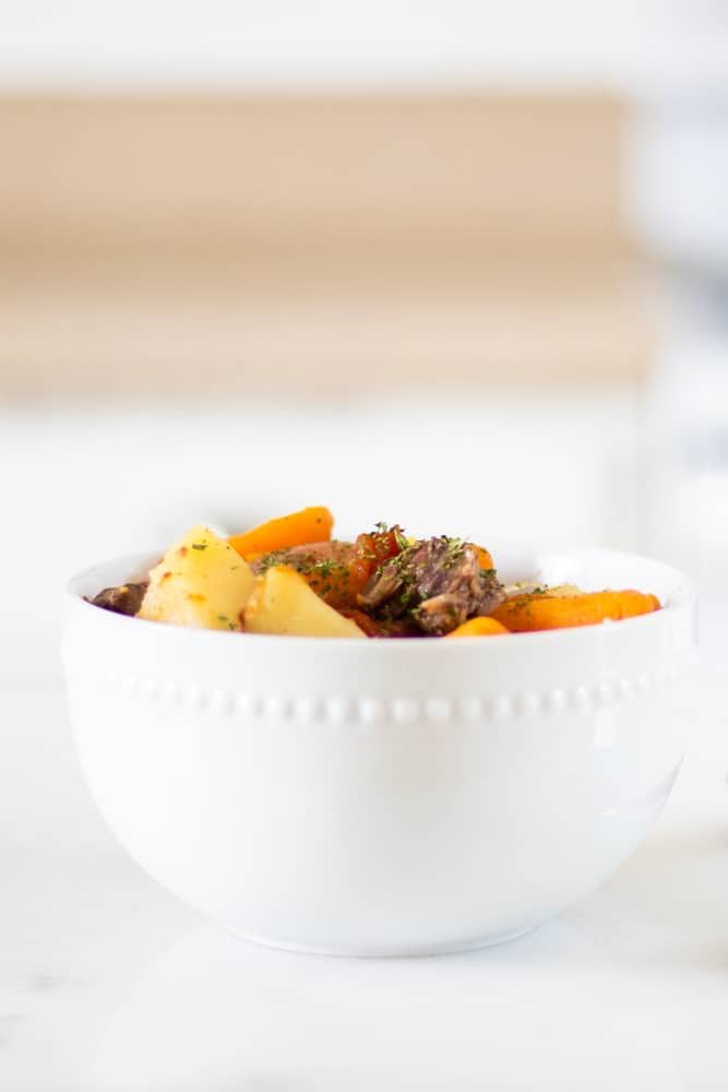 white bowl of homemade beef stew recipe with decorative greens sprinkled on top.