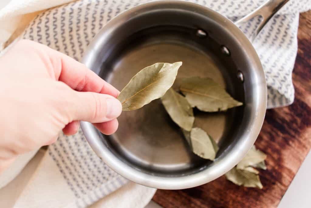 Adding bay leaves to water in a pan.