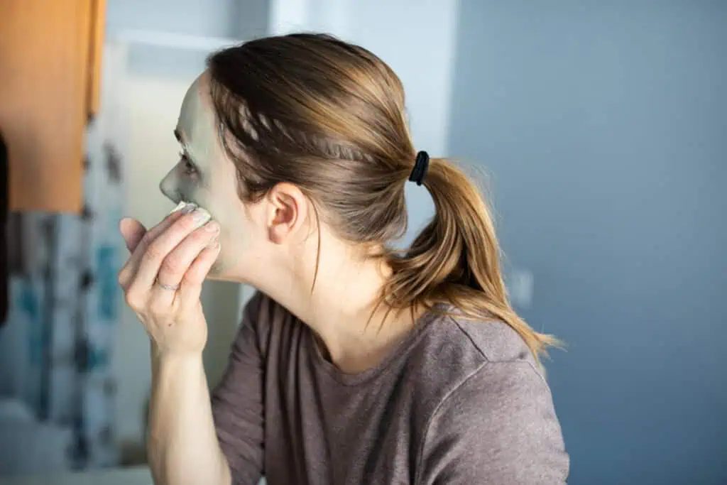 The author, the studio, applying a bentonite clay mask to her face in the bathroom with her hands.