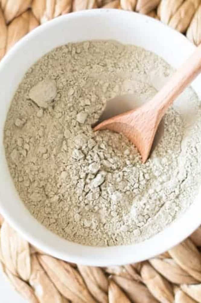 Bentonite clay in white glass bowl with a wooden spoon in it.