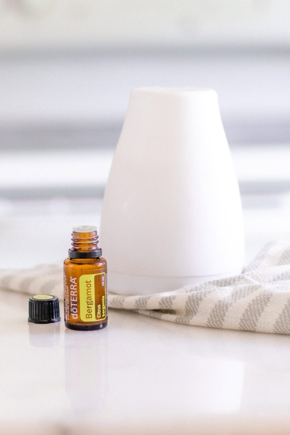 Bergamot oil and white diffuser on white marble.