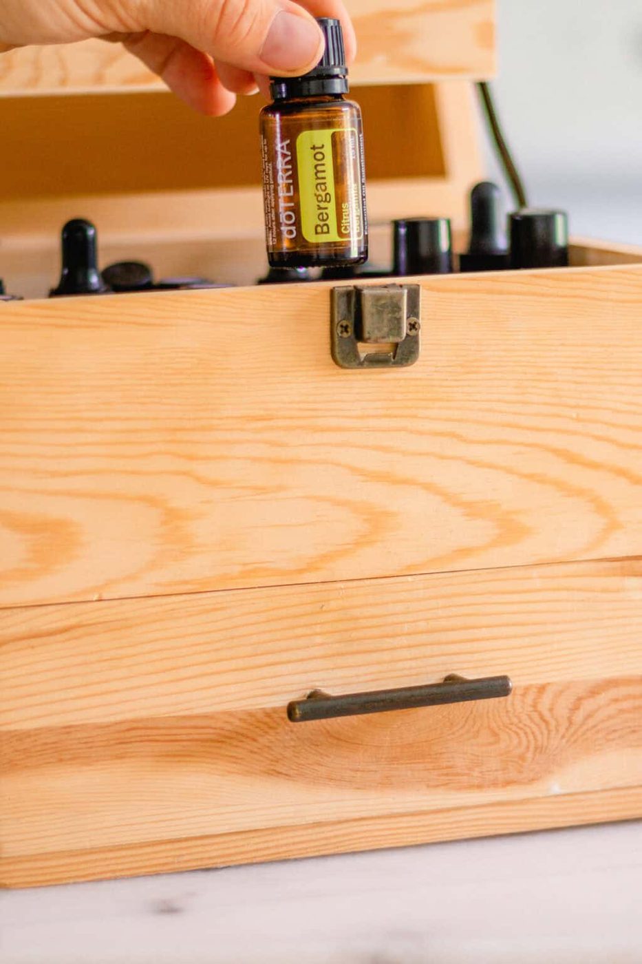 Picking up a bergamot oil out of a wooden essential oil storage box.