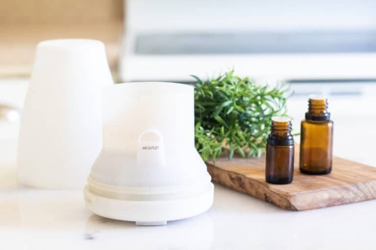 White essential oil diffuser on table with amber colored essential oil bottles and rosemary sprigs.