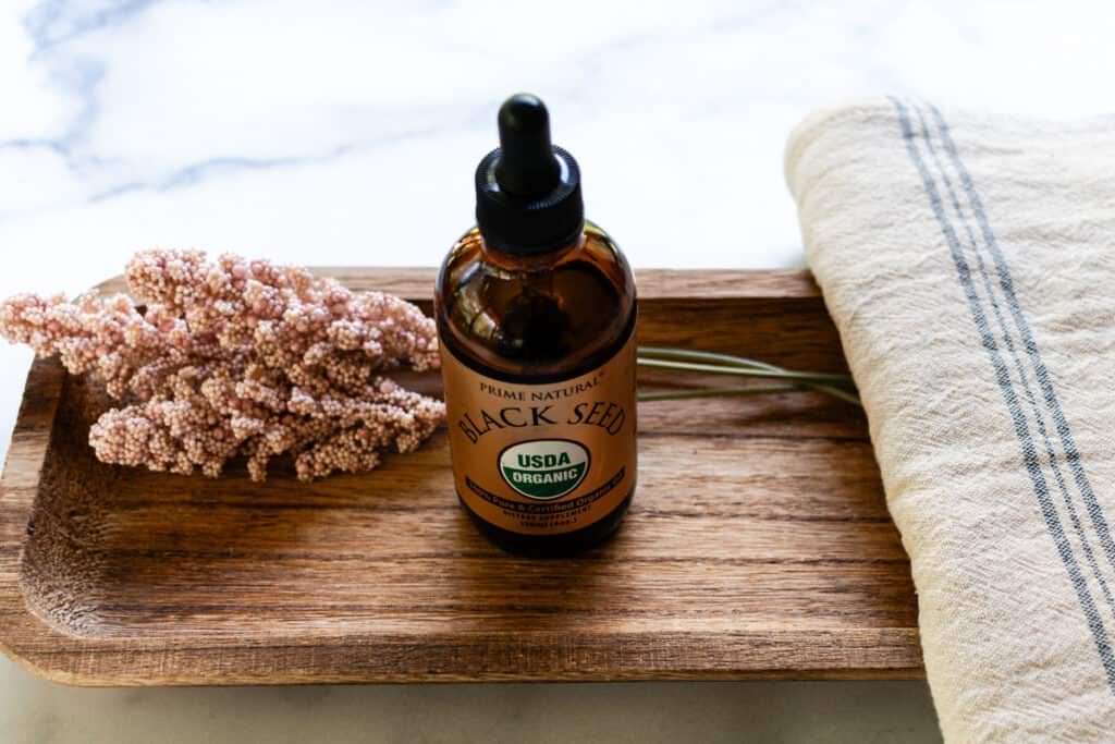 A dropper bottle of black seed oil with pink flowers in the background.