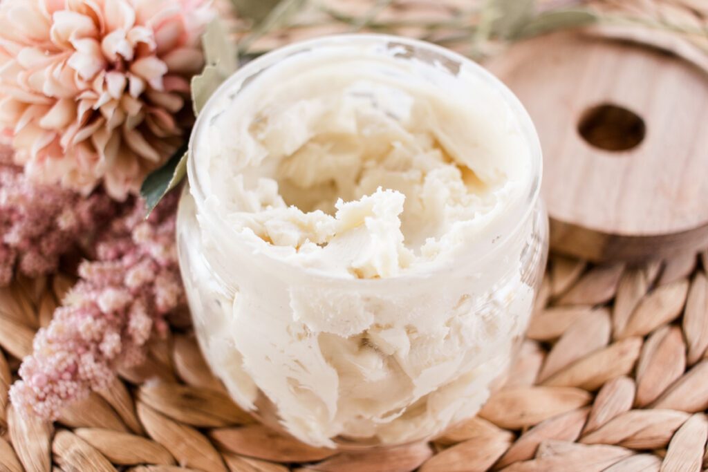 Whipped body cream in a pot beside pretty flowers.