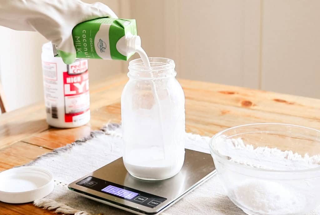 Pouring coconut milk into a jar sitting on a kitchen scale.