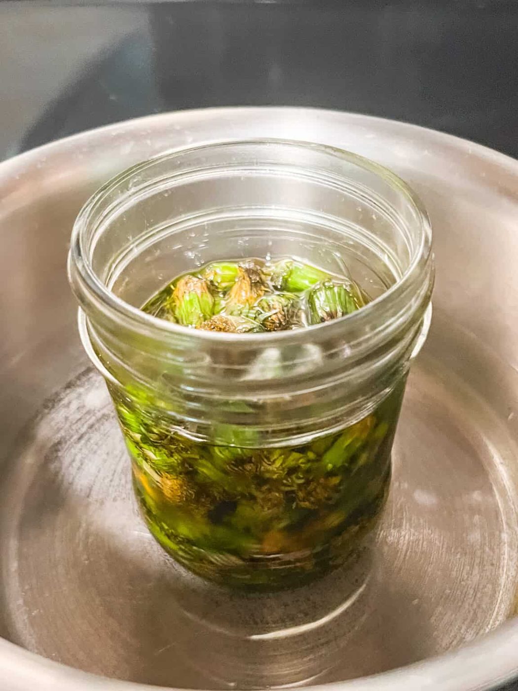 A jar of oil and dandelions in a pot of water.