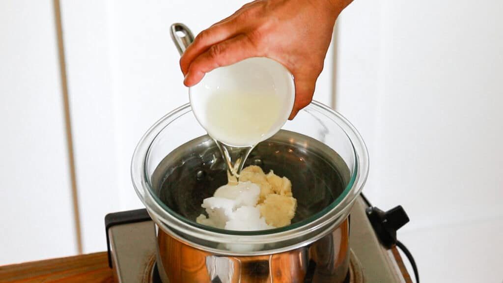 Pouring sunflower oil into a double boiler with the butters and coconut oil to make deodorant cream.