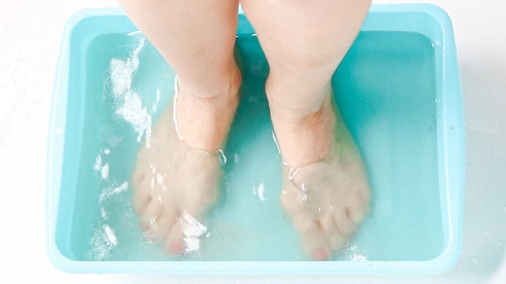 Feet soaking in a foot bath in a teal water basin.