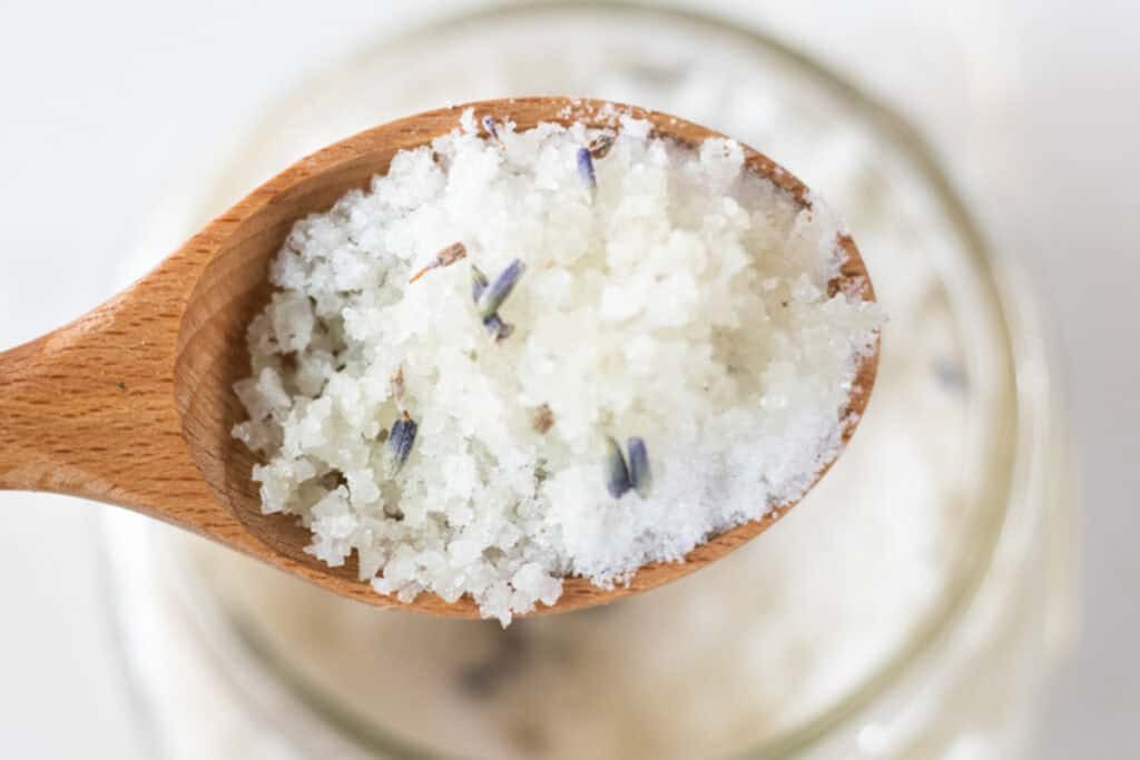 A spoonful of detoxifying foot bath being help up over a jar of foot bath.