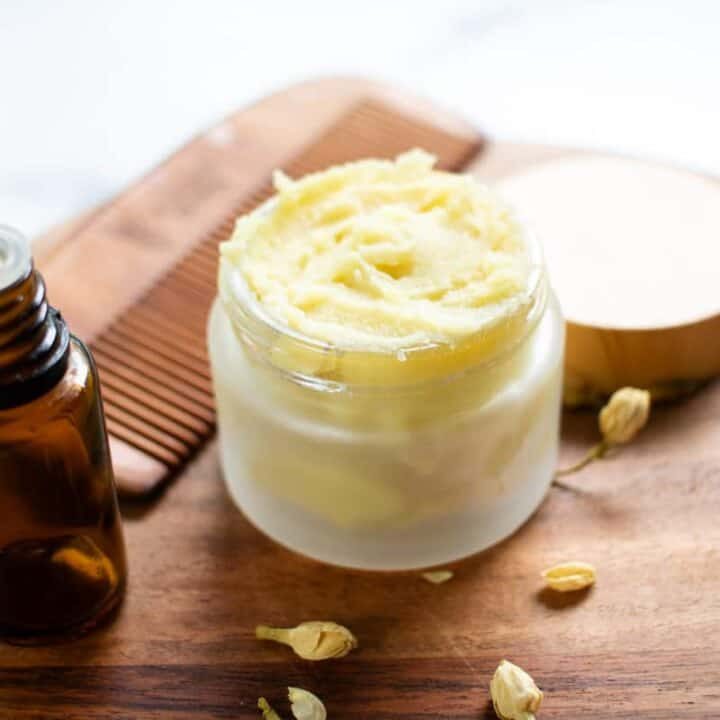 A homemade beard butter in a beautiful glass container with a beard comb in the background.