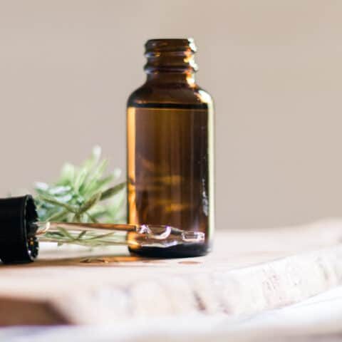 A homemade beard growth oil in an amber colored dropper bottle with the dropper top laying next to it.