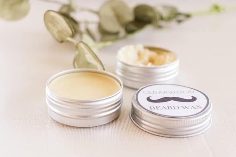 Beard pomade/beard wax in metal tins with green leaves in background.