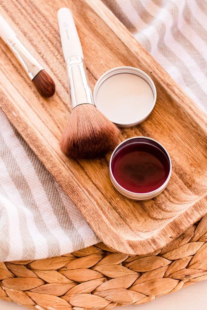 A pot of diy blush cream and brush on a wooden board.