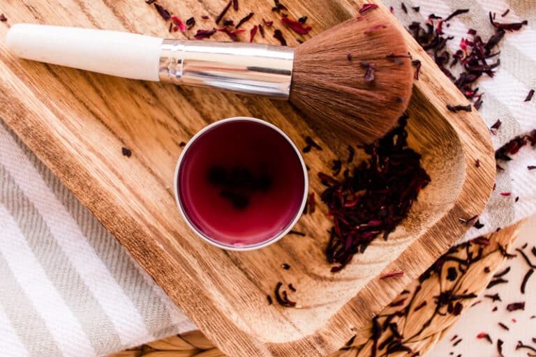 A pot of diy blush cream and a blusher brush on a wooden board.
