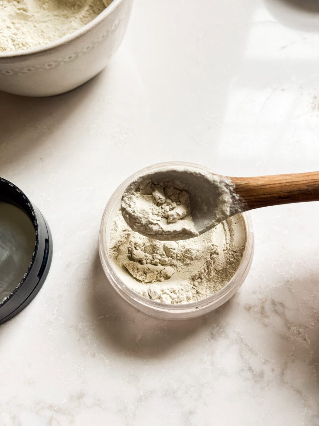 Scooping body powder into a storage jar with a spoon.