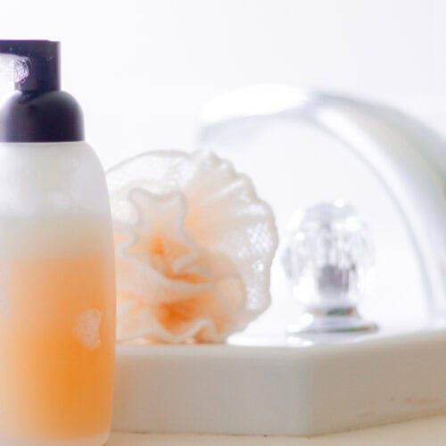 A bottle of natural body wash with a loofah and sink in the background.