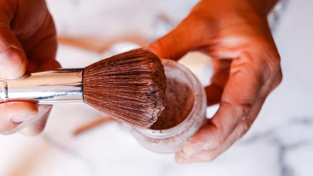 Dabbing the bronzer brush into the makeup container.