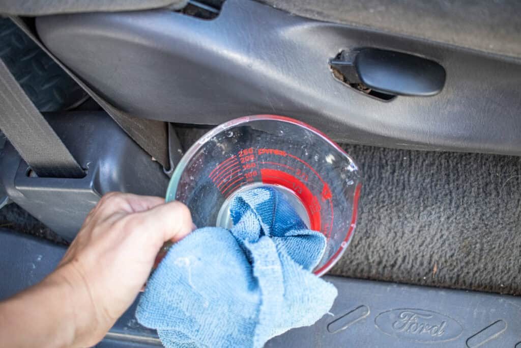 A measuring cup with soap water for cleaning leather car seats.