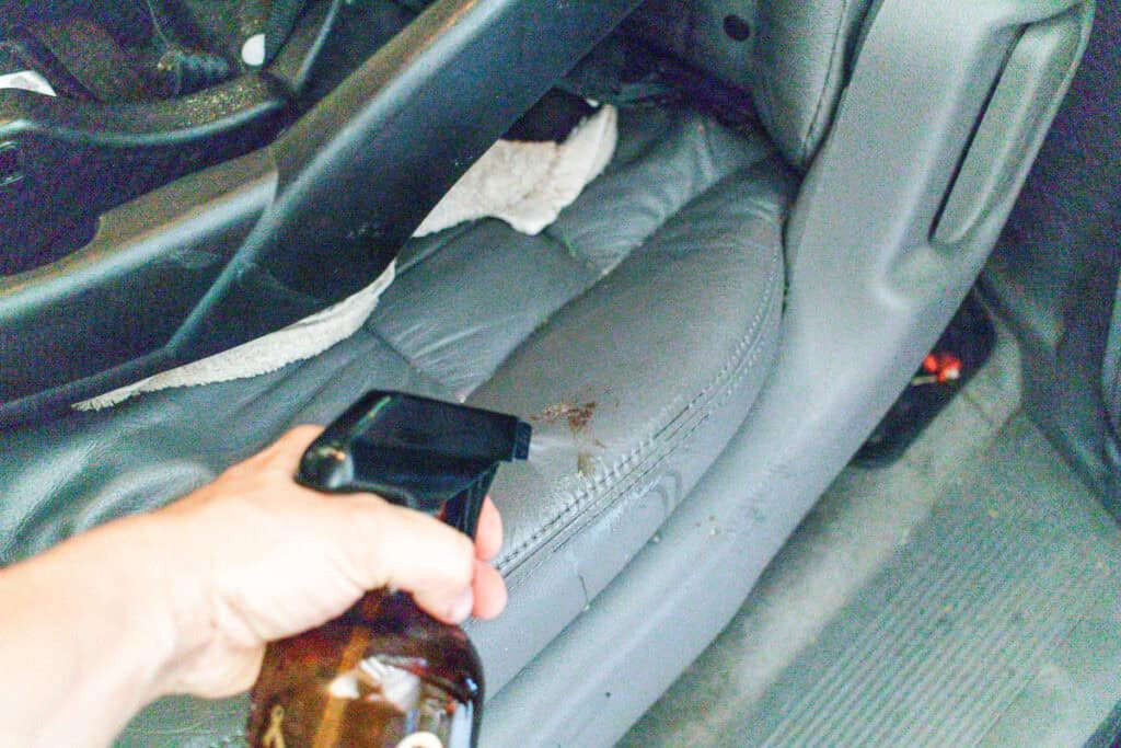 Spraying a leather car seat with a spray bottle of soap water.