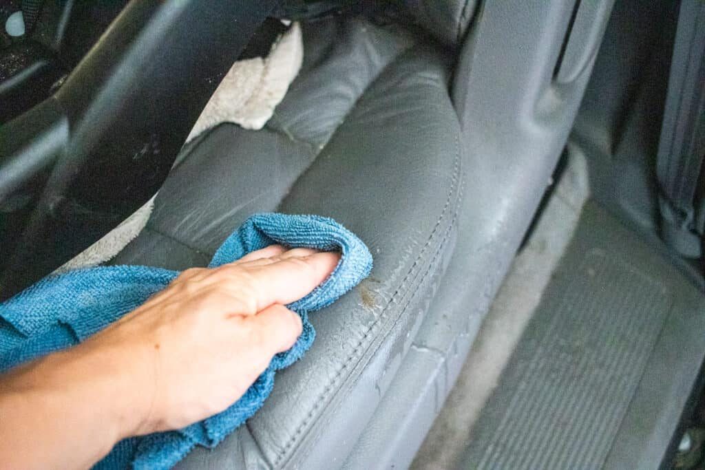 Wiping a leather car seat with a microfiber cloth.