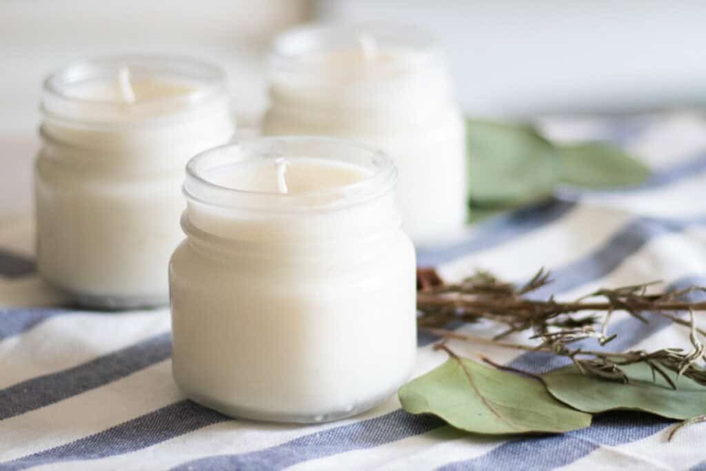Homemade Christmas candles on a blue and white striped towel with greenery.