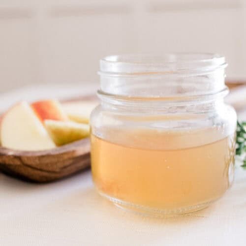 Homemade clarifying shampoo in shallow glass jar on white tablecloth.