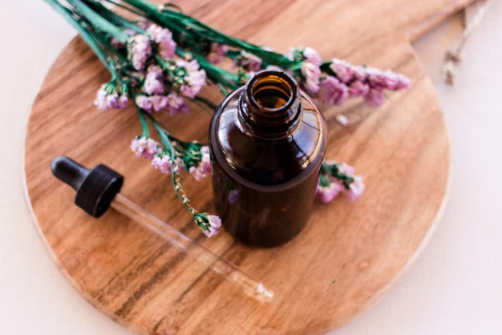 The mixed facial cleansing oil on a round wooden tray on a white vanity with colorful flowers next to it.