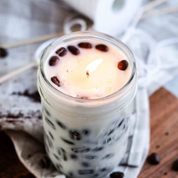 A DIY Coffee candle burning in a room with whole coffee beans spread around it.