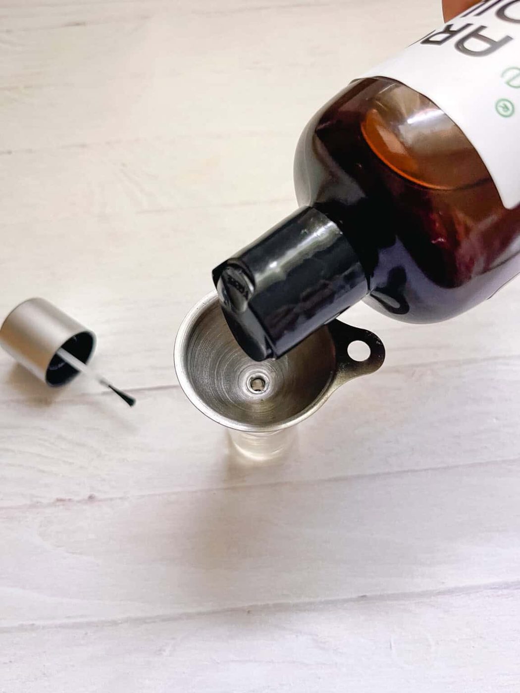 Pouring oil into an empty nail polish bottle with a small funnel.