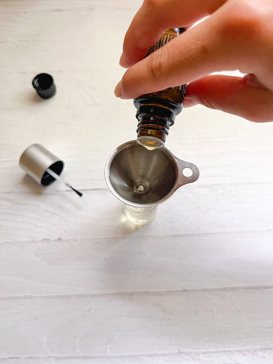 Dropping essential oils into a nail polish bottle with a small funnel.