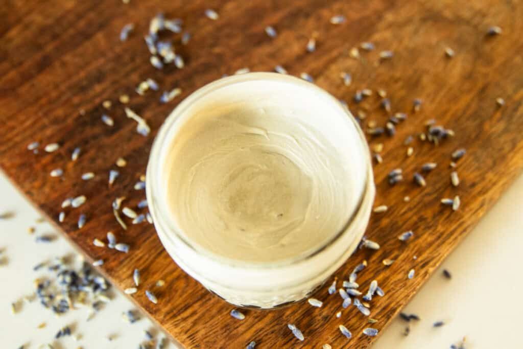 A jar of homemade diaper cream on a wooden board surrounded by lavender buds.