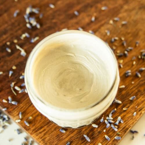 A jar of homemade diaper cream on a wooden board surrounded by lavender buds.