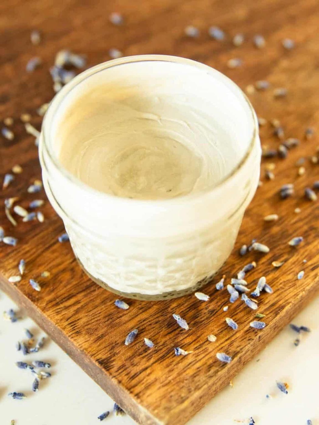 A jar of diaper cream on a wooden board with dried lavender buds.