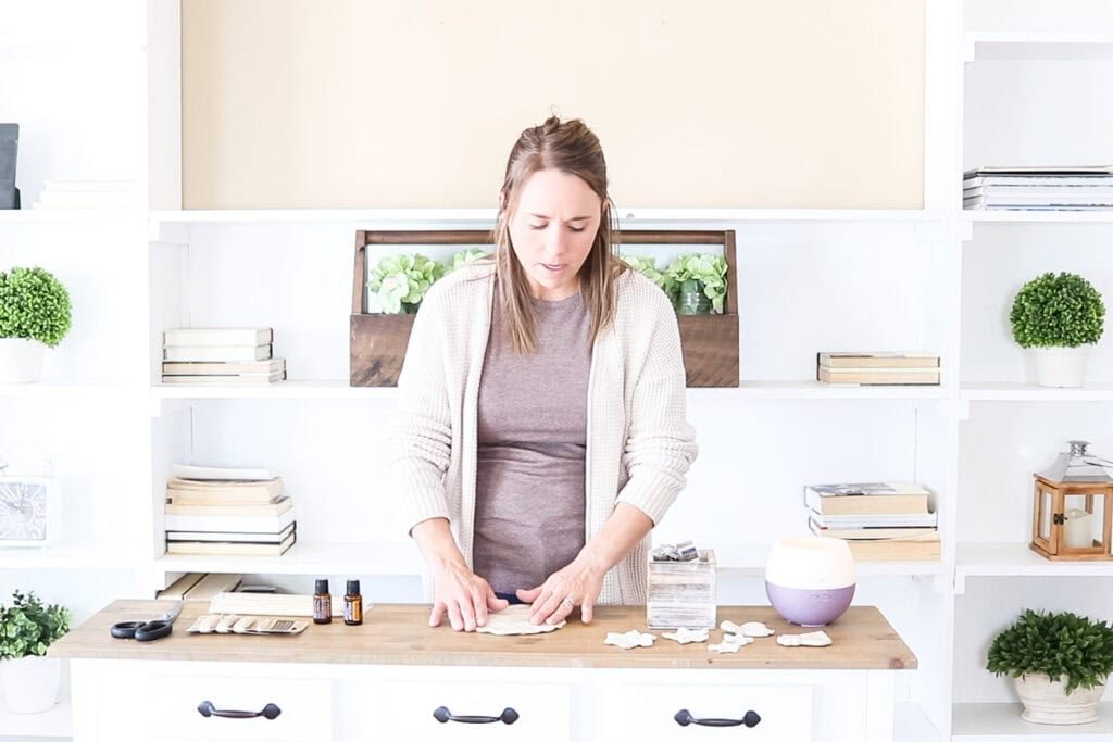 Standing at a counter pressing a ball of clay into a patty.