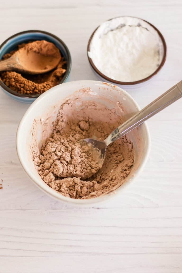 Dry shampoo mixed in a bowl with extra bowls of arrowroot powder and cocoa powder next to it.