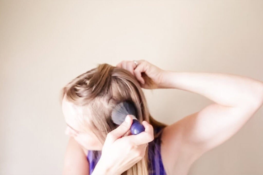Applying dry shampoo to the scalp using a fluffy makeup brush.