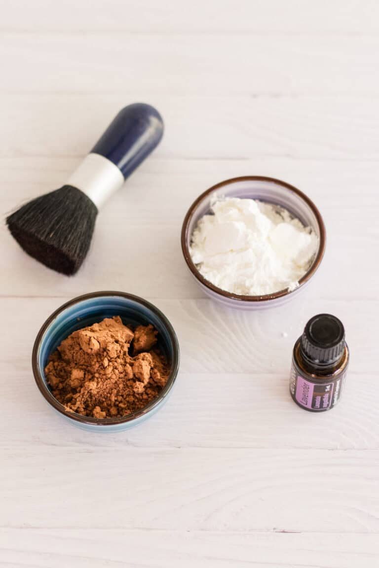 Dry shampoo ingredients: arrowroot powder, cocoa powder, and essential oil with a makeup brush for application.