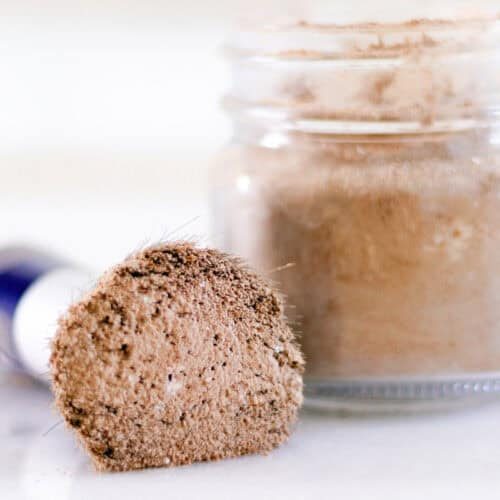 Dry shampoo on a makeup brush with a glass jar of dry shampoo sitting next to it.
